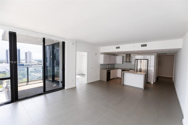 interior space with stainless steel refrigerator, decorative backsplash, black dishwasher, expansive windows, and wall chimney range hood