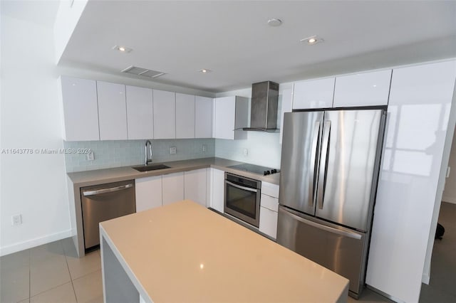 kitchen with stainless steel appliances, sink, wall chimney range hood, and white cabinetry