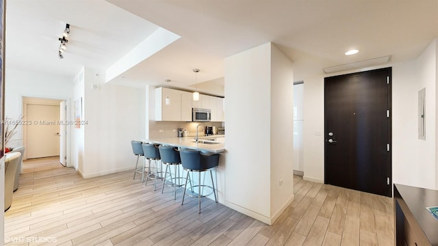 kitchen featuring white cabinets, sink, kitchen peninsula, decorative light fixtures, and light hardwood / wood-style floors