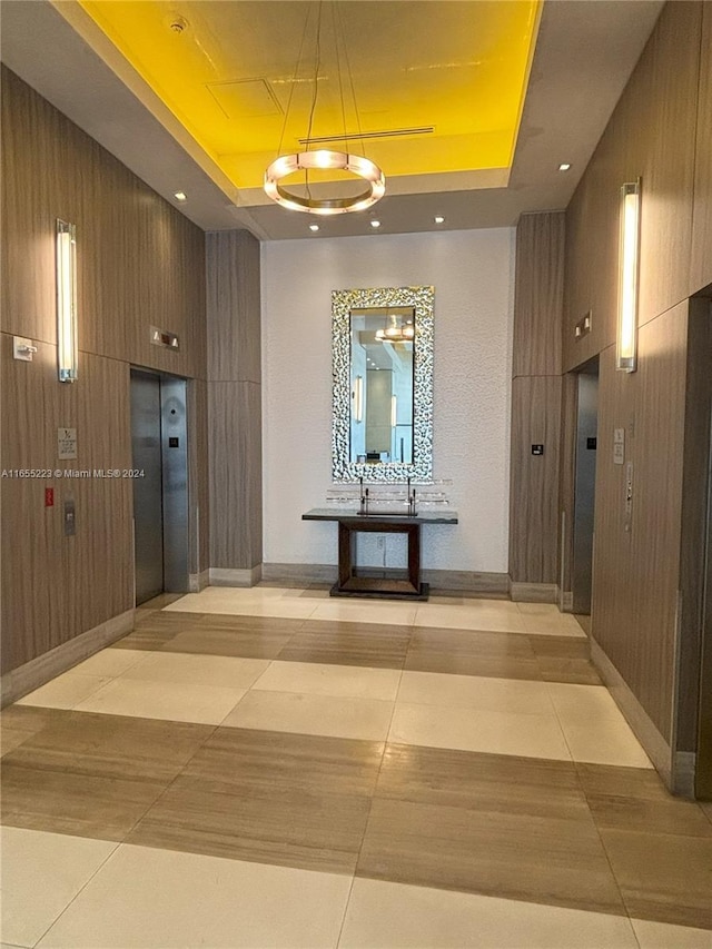 corridor featuring a raised ceiling, wood walls, and elevator