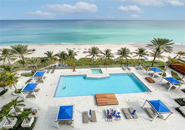 view of swimming pool featuring a water view, a view of the beach, and a patio