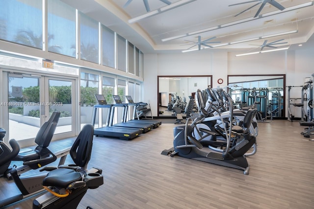 exercise room featuring a towering ceiling, hardwood / wood-style floors, ceiling fan, and french doors