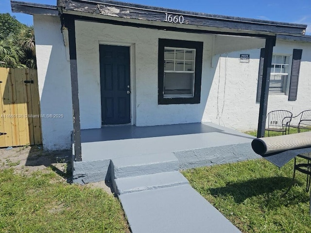 doorway to property featuring stucco siding and fence