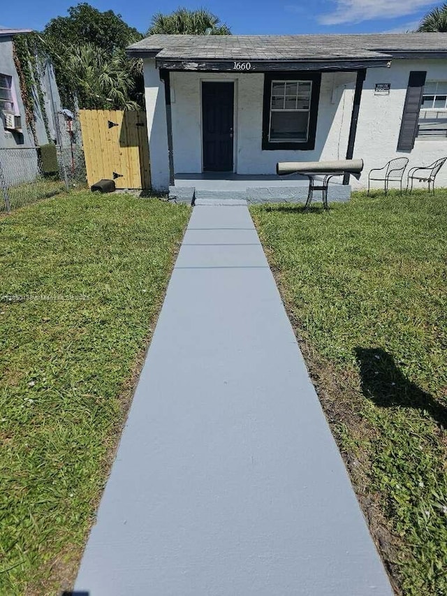 entrance to property with stucco siding, fence, and a lawn