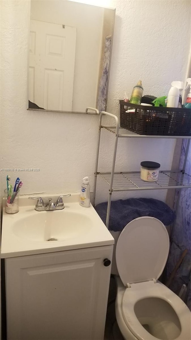bathroom featuring toilet, vanity, and a textured wall
