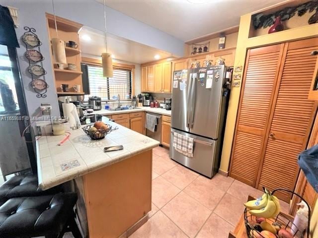 kitchen featuring kitchen peninsula, sink, hanging light fixtures, appliances with stainless steel finishes, and light tile patterned flooring