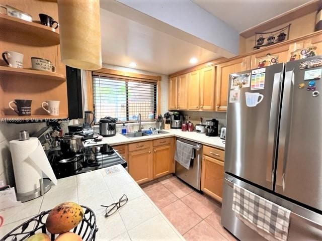 kitchen featuring appliances with stainless steel finishes, tile counters, sink, light brown cabinets, and light tile patterned flooring