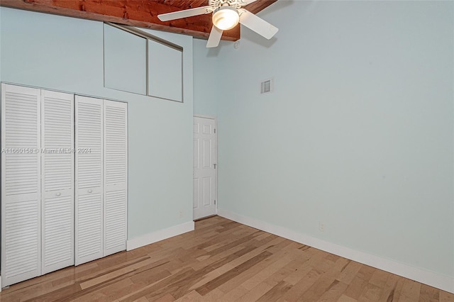 unfurnished bedroom with beamed ceiling, a closet, wood-type flooring, ceiling fan, and a towering ceiling