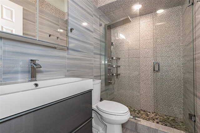 bathroom with tile walls, toilet, a shower with door, and vanity