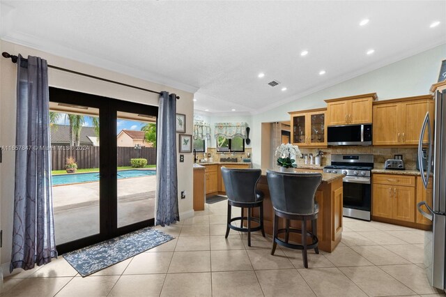 kitchen with light tile patterned floors, a kitchen breakfast bar, vaulted ceiling, a kitchen island, and appliances with stainless steel finishes