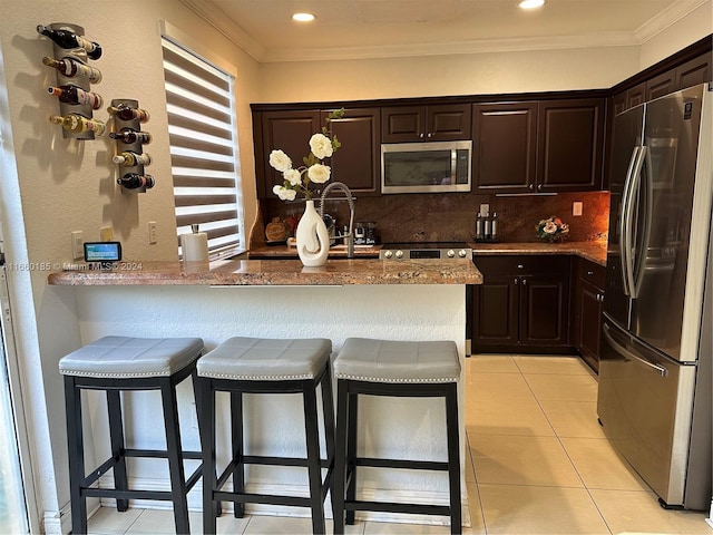 kitchen featuring light tile patterned floors, stainless steel appliances, a kitchen breakfast bar, kitchen peninsula, and stone countertops