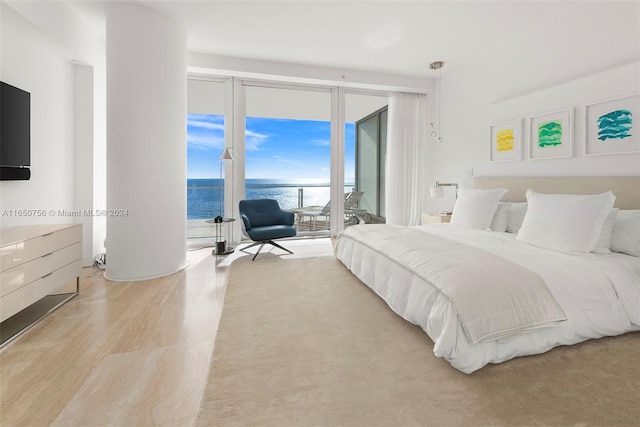 bedroom with a wall of windows, a water view, light wood-type flooring, and access to outside