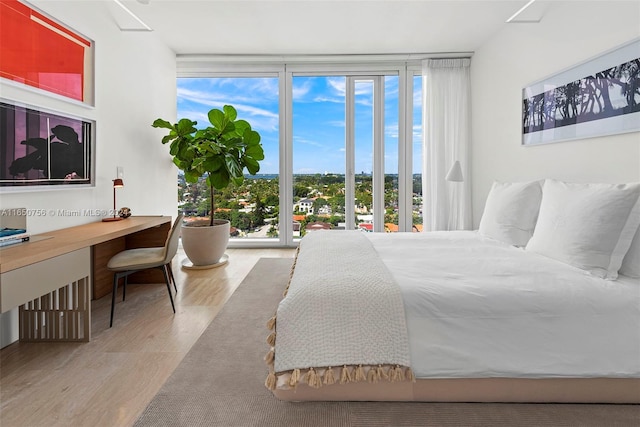 bedroom with a wall of windows, light hardwood / wood-style flooring, and multiple windows