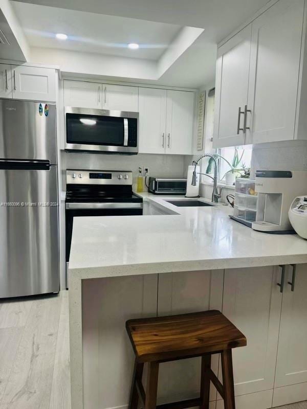 kitchen with kitchen peninsula, a breakfast bar, stainless steel appliances, sink, and white cabinets