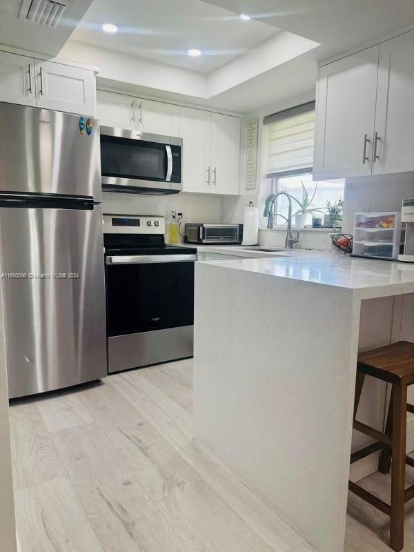 kitchen with light wood-type flooring, stainless steel appliances, a tray ceiling, sink, and white cabinetry