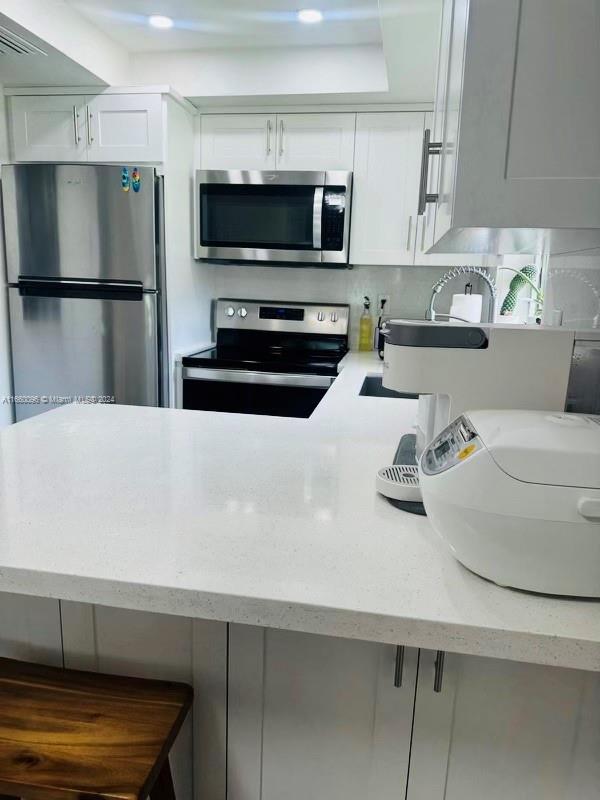 kitchen with light stone countertops, stainless steel appliances, and white cabinetry