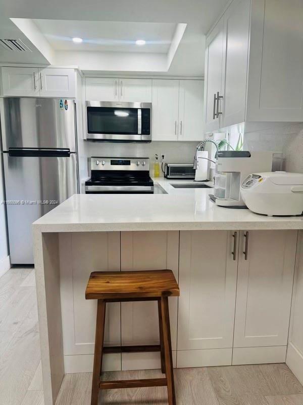 kitchen featuring white cabinetry, sink, stainless steel appliances, a breakfast bar, and light wood-type flooring