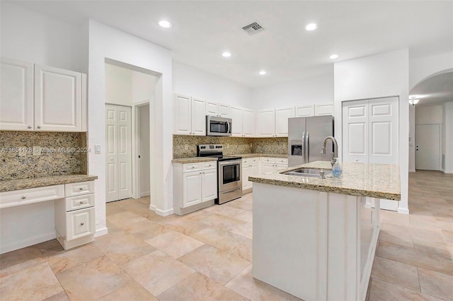 kitchen featuring appliances with stainless steel finishes, white cabinetry, light stone countertops, a center island with sink, and sink