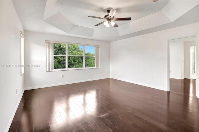 spare room with dark wood-type flooring, ceiling fan, baseboards, and a raised ceiling
