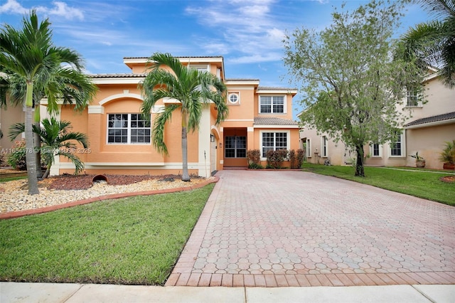 mediterranean / spanish home featuring a front yard, a tile roof, decorative driveway, and stucco siding
