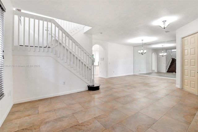 empty room featuring arched walkways, baseboards, a notable chandelier, and stairway
