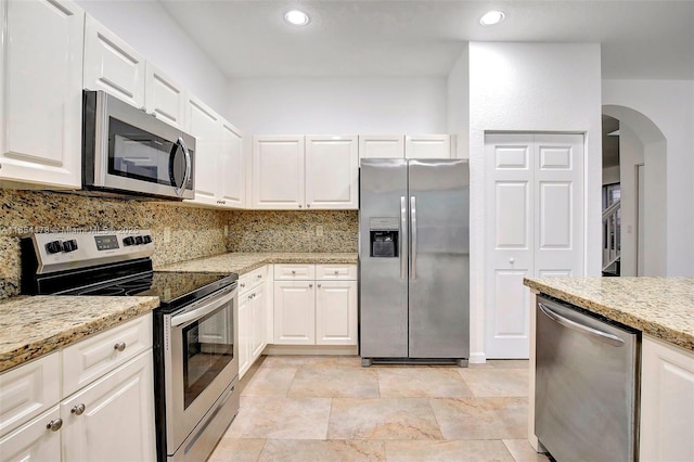 kitchen featuring tasteful backsplash, light stone counters, white cabinets, stainless steel appliances, and arched walkways