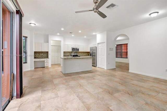 kitchen with ceiling fan, an island with sink, white cabinetry, appliances with stainless steel finishes, and decorative backsplash