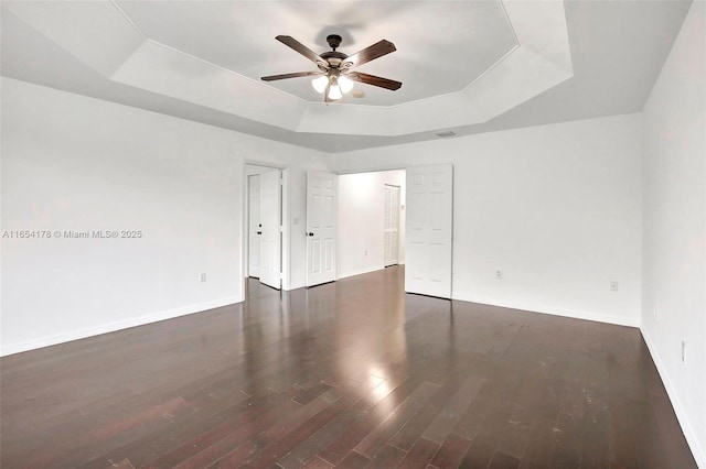 empty room with a tray ceiling, ceiling fan, wood finished floors, and baseboards