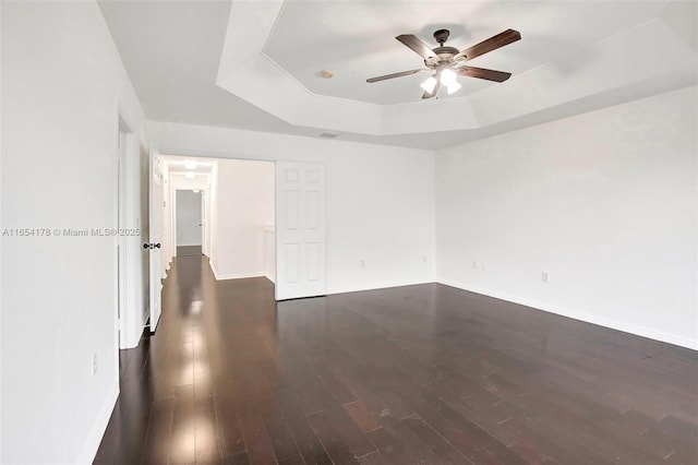 unfurnished room featuring a tray ceiling, ceiling fan, baseboards, and dark wood-style flooring