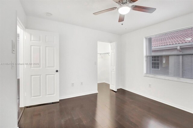 unfurnished bedroom with ceiling fan, a closet, dark wood-type flooring, and a walk in closet