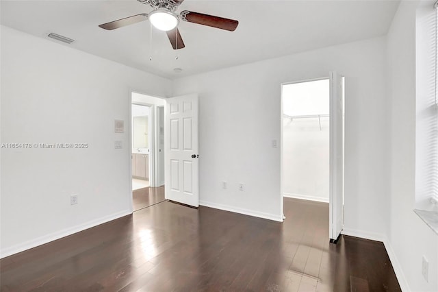 unfurnished bedroom featuring a walk in closet, visible vents, dark wood-style flooring, and baseboards