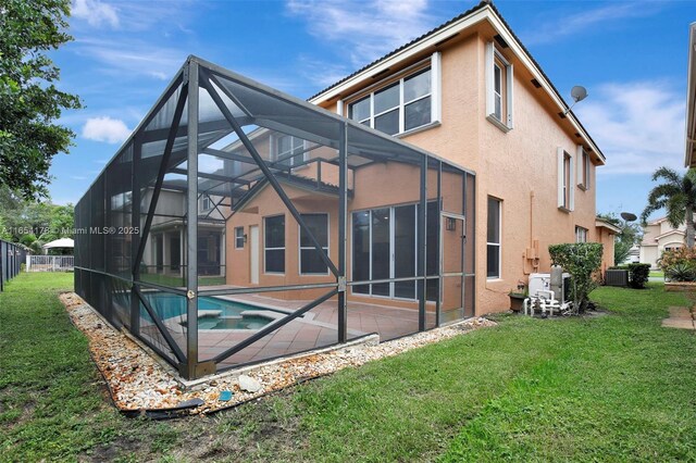 rear view of house with cooling unit, glass enclosure, an in ground hot tub, and a lawn