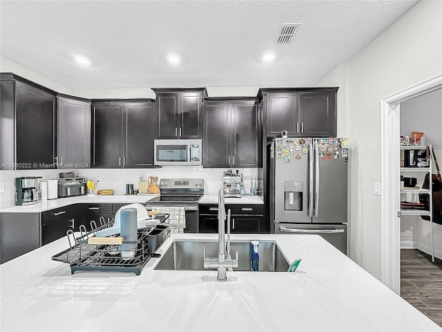 kitchen with a textured ceiling, dark hardwood / wood-style flooring, appliances with stainless steel finishes, sink, and decorative backsplash