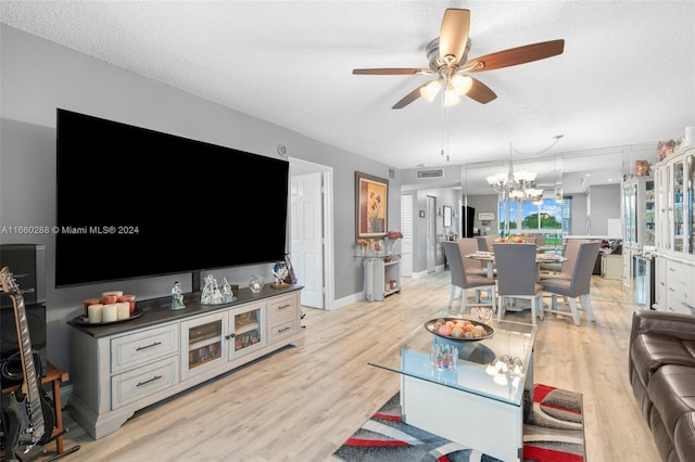 living room featuring ceiling fan with notable chandelier, light wood-type flooring, and a textured ceiling