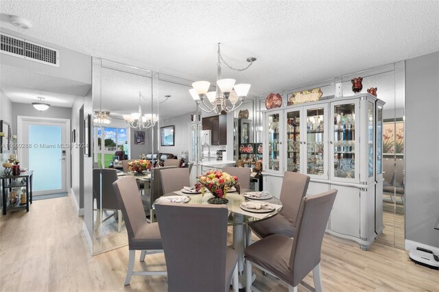 dining area with a textured ceiling, an inviting chandelier, and light hardwood / wood-style flooring