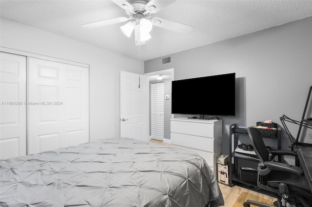 bedroom featuring a textured ceiling, a closet, light hardwood / wood-style flooring, and ceiling fan