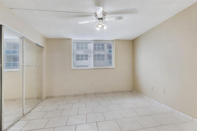 unfurnished bedroom featuring a textured ceiling, light tile patterned floors, ceiling fan, and a closet