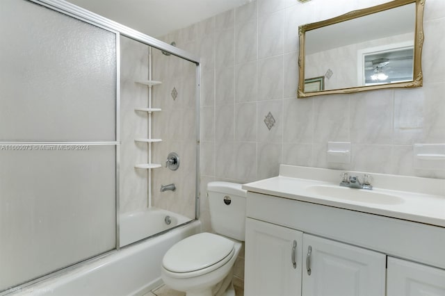 full bathroom featuring shower / bath combination with glass door, vanity, toilet, and tile walls