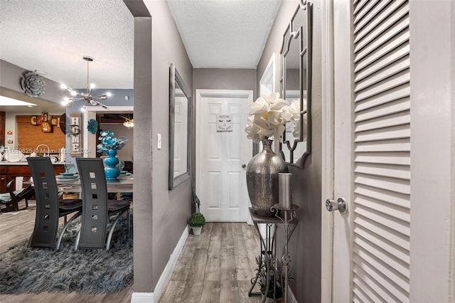 hallway with a textured ceiling, hardwood / wood-style floors, and an inviting chandelier