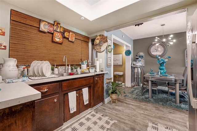 interior space with light wood-type flooring, decorative light fixtures, a notable chandelier, sink, and dark brown cabinets