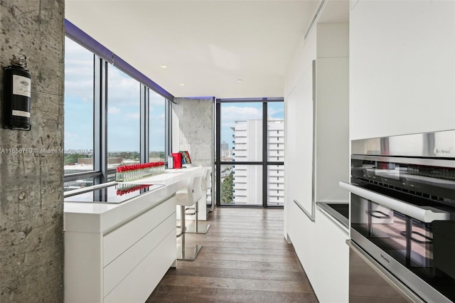 kitchen with a wall of windows, white cabinets, dark hardwood / wood-style floors, and oven