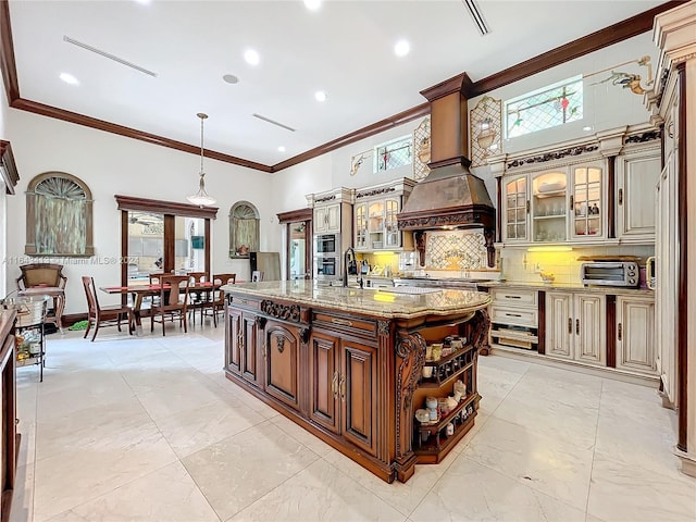 kitchen with decorative backsplash, crown molding, light stone countertops, and a kitchen island with sink