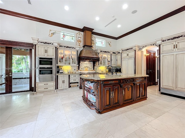 kitchen with sink, tasteful backsplash, cream cabinets, an island with sink, and ornamental molding