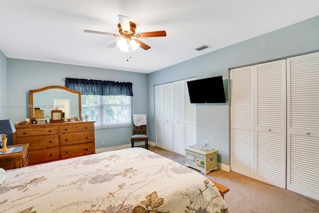 bedroom with ceiling fan, light carpet, and multiple closets