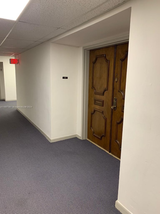 hallway with a paneled ceiling and dark colored carpet