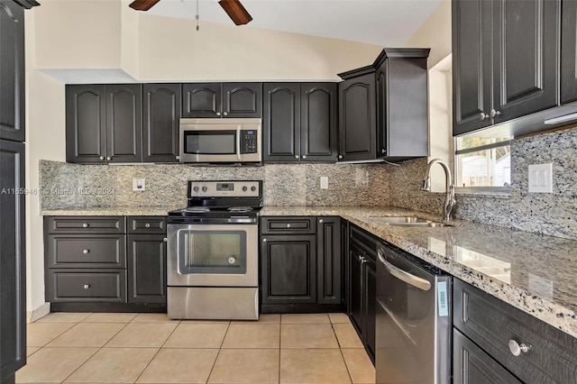 kitchen featuring vaulted ceiling, light stone countertops, stainless steel appliances, sink, and ceiling fan