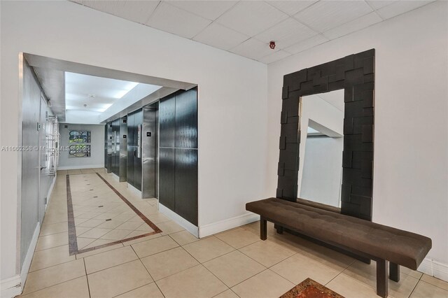 hall with light tile patterned floors and a paneled ceiling