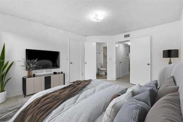 bedroom featuring a textured ceiling, light wood-type flooring, and ensuite bath