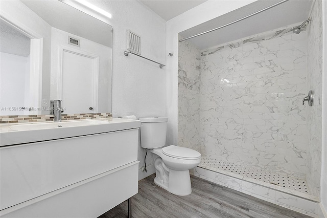 bathroom featuring vanity, a tile shower, wood-type flooring, and toilet