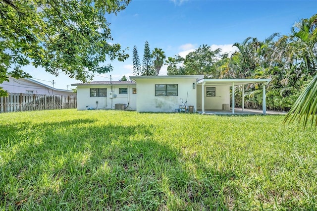 rear view of property with a patio area, a yard, a carport, stucco siding, and fence